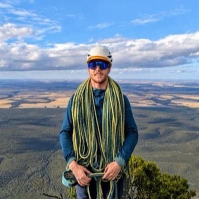 Evan on a summit with a long rope coiled over his shoulders, farmland stretching to the horizon.