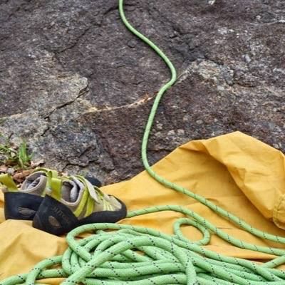 Climbing shoes and a coiled green rope on a yellow rope bag at the foot of the rock.