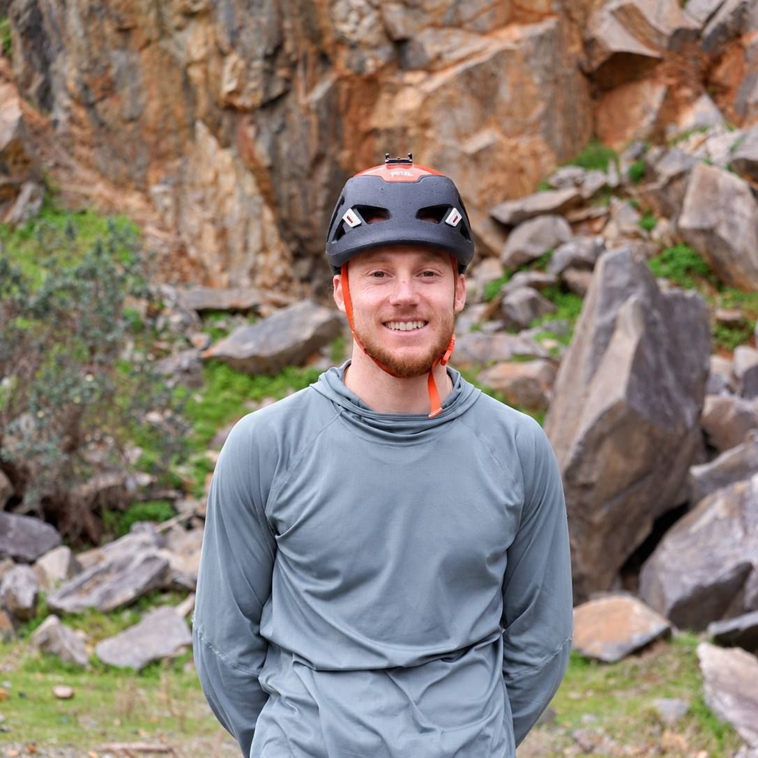 Evan smiling in his climbing helmet in front of a rocky crag in the Perth Hills.